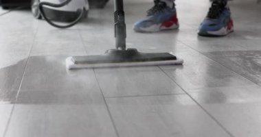 Buharlı paspas kirli fayansları temizlerken süzülüyor. Sıcak cihaz yüzeydeki lekeleri temizliyor. Geniş modern mutfak dairesindeki lekeleri temizliyor.