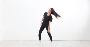 Siyah elbiseli kadın stüdyoda dans ederken uzun saç sallanıyor. Dansçı güçlü sokak stili yavaş çekim gösterirken vücudunu keskin bir şekilde hareket ettirir.