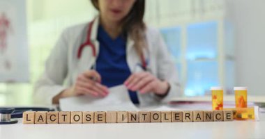 Masa formundaki tahta küpler laktoz intoleransı hastanın durumunu gösteriyor. Kadın doktor haplar için reçete yazıyor. Yavaş çekim