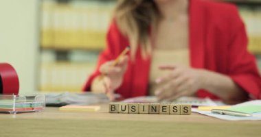 Minyatür ahşap bloklar masada iş dünyası oluşturur. İş kadını masada oturuyor ve şirket büyümesi için stratejik fikirleri dikkatlice kaydediyor.