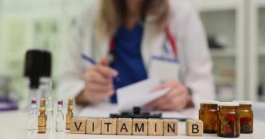 Kadın doktor masada oturan vitaminler için reçete yazıyor. Tahta bloklar hasta için tabletlerle dolu kapların yanında B vitamini terimi oluşturur.