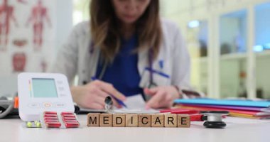 Tahta bloklara, kan basıncı monitörü haplarıyla ve klinikteki steteskopla sağlık sigortası yaz. Kadın doktor, iş yerinde oturan hasta kayıtlarını dolduruyor.