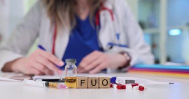 Hastanedeki şırınga ve ilaçlarla dijital termometrenin yanındaki tahta bloklarda FUO kısaltması. Kadın doktor klinikte hastanın test sonuçlarını analiz eder.