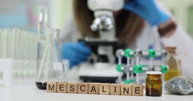 Tahta bloklardaki meskalin kelime, cam kaplama ve moleküler yapı modeli laboratuvarda. Kadın kimyager mikroskop altında psikedelik madde araştırması yapıyor.