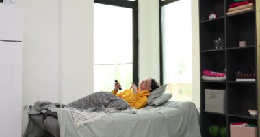 Genç bir kadın yatağa uzanmış kendini kötü hissederken uzaktan kumandayla televizyon kanallarını değiştiriyor. Tembel kadın evdeki rahat kanepede dinlenirken televizyon izler.