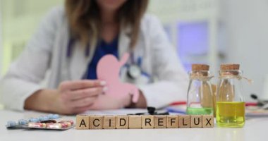 Tahta küpler renkli sıvılarla cam şişelerin yanında duran asit reflüsünü büyüler. Doktor, hasta için hastalık tedavisini açıklayan mide modelini tutuyor