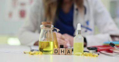 Tahta küpler sağlık masasında DHA sözcüğünü heceler. Doktor, beslenme danışmanlığı sırasında şişedeki balık yağı takviyesi kapsüllerini inceleyen bir not yazıyor.