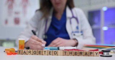 Tahta küplerin heceleme cümlesi klinik masasında hedeflenmiş terapi. Kadın onkolog, kanser tedavisi sırasında şırınga ve hapları kontrol etme planı yazıyor.