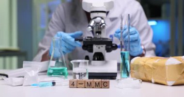 Tahta küplerin kod 4 MMC 'si renkli laboratuvar camlarının yanında. Bilim adamları test tüpleri ve laboratuardaki sıvı örnekleriyle mikroskobu ilaç paketinin yakınına ayarlıyorlar.