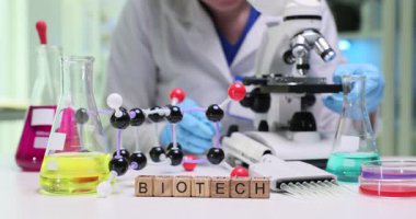 Tahta küpler biyoteknoloji kelimesini renkli molekül modelinin yanında heceler. Laboratuvardaki bilim adamı genetik mühendisliği ve ilaç yeniliklerini araştırıyor.