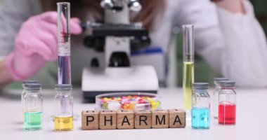 Tahta küpler farma 'yı parlak laboratuvar masasında büyülüyor. Eldivenlerdeki eczacı, mikroskop altında ilaç örnekleri hazırlayan renkli uyuşturucu çözümlerini test ediyor