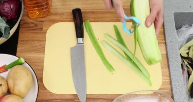 Eller, evde yemek pişirmek için taze kabağı ince kurdelelere ayırmak için aynasızları kullanır. Kesme tahtasında kabakların soyulmuş şeritleri var.