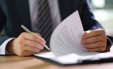 Takım elbiseli odaklanmış bir birey cilalı bir masadaki bir yığın belgeyi inceliyor. Öğleden sonranın ılık ışığı içeri süzülüp verimli bir atmosfer yaratıyor..