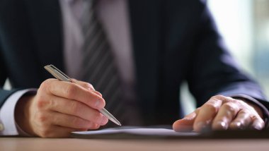 İyi giyimli bir adam parlak bir ofiste parlak bir kağıdın üzerine gümüş bir kalemle yazarken dikkatle odaklanır. Güneş ışığı, üretkenlik ve kararlılığı yansıtarak içeri akar..