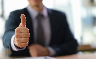 Hareketli bir ofis ortamında, şık bir takım elbise giymiş bir adam başarılı bir tartışmanın ardından coşkulu bir şekilde onaylama, onay ve pozitiflik sinyali veriyor. Davranışları güven yayıyor..