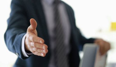 Bir işadamı, iyi aydınlatılmış bir ofiste dostça el sıkışmak için elini uzatır. Atmosfer hoş karşılayıcı ve profesyonelce, yeni başlangıçları ve bağlantıları vurguluyor.