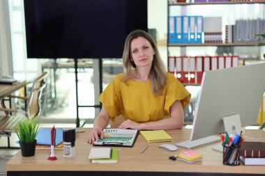 Kendine güvenen bir kadın, çağdaş bir ofiste düzenli bir masada oturuyor, belgeler üzerinde çalışıyor ve notlar alıyor. Parlak renkler ve düzenli raflar verimli bir atmosfer yaratır..