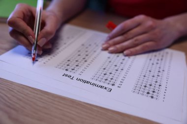 Bir öğrenci soruları test kağıdında cevaplamaya odaklanır, cevapları kırmızı kalemle dikkatlice işaretler. Ilık ışık rahat bir çalışma ortamı yaratıyor ve odağı arttırıyor..