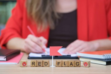 Hareketli bir ofis ortamında, bir kadın renkli kalemlerle notlar yazmaya odaklanırken, kırmızı bayraklar arasında kırmızı bayraklar beliriyor. Etrafını parlak defterler ve kırtasiyeler sarmış..