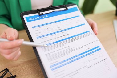 Sıcak bir ofiste, bir kişi elinde not almaya hazır bir kalemle sigorta formunu dikkatle inceler. Ortam sakin, bu da kapsama seçenekleri hakkında önemli bir tartışma olduğunu gösteriyor..