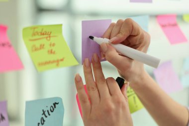 Eller canlı bir beyin fırtınası sırasında aktif bir şekilde yapışkan bir nota yazıyorlar. Parlak renkler arkaplanı doldurur, yaratıcılığa ve işbirliğine ilham verir.