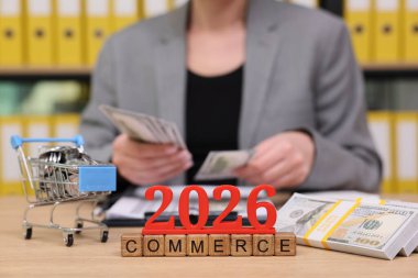 Canlı bir ofiste, bir iş adamı 2026 'daki ticaret eğilimlerini düşünürken para birimini analiz eder. Bir alışveriş arabası ve yığınla para yatırım fırsatlarını ön plana çıkarıyor.