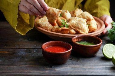 Samosa - tuzlu dolgulu kızarmış / fırında hamur işi, popüler Hint aperatifleri, baharatlı kasede servis edilen ve rustik arka planda taze kişniş
