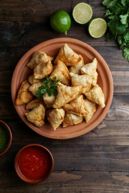 Samosa - tuzlu dolgulu kızarmış / fırında hamur işi, popüler Hint aperatifleri, baharatlı kasede servis edilen ve rustik arka planda taze kişniş