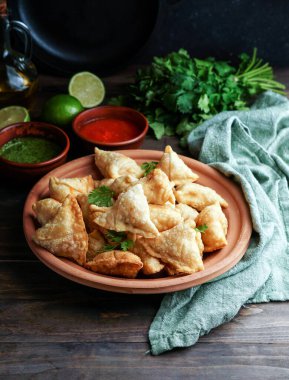Samosa - tuzlu dolgulu kızarmış / fırında hamur işi, popüler Hint aperatifleri, baharatlı kasede servis edilen ve rustik arka planda taze kişniş