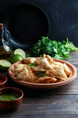 Samosa - tuzlu dolgulu kızarmış / fırında hamur işi, popüler Hint aperatifleri, baharatlı kasede servis edilen ve rustik arka planda taze kişniş