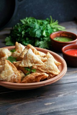 Samosa - tuzlu dolgulu kızarmış / fırında hamur işi, popüler Hint aperatifleri, baharatlı kasede servis edilen ve rustik arka planda taze kişniş