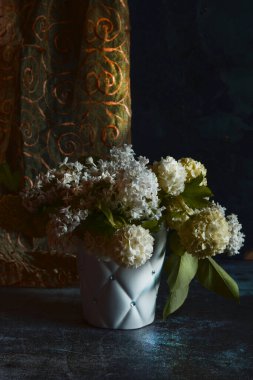 Beyaz bir buket Viburnum ve leylak çiçeğinin karışımı, koyu bir arka planda beyaz bir kapta..