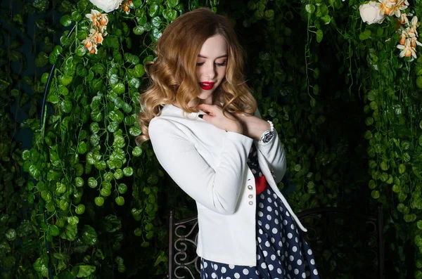 드레스를 입고 하얀 재킷을 입은 곱슬머리의 소녀가 정원을 걷고 있습니다.. — 스톡 사진