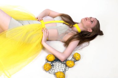 Sarı elbiseli bir kız beyaz bir zeminde limonlarla yatıyor..