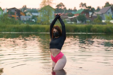 Siyah tıbbi maskeli güzel bir kadın nehirde duruyor. Salgında dinleniyor..