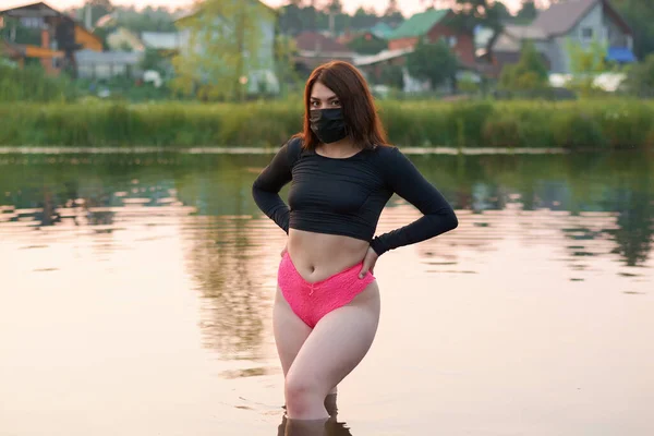 Een mooie vrouw met een zwart medisch masker staat in de rivier.rest in de pandemie. — Stockfoto