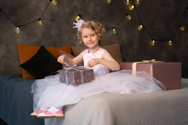 Una niña con un vestido rosa y una corona en la cama con regalos —  Fotos de Stock