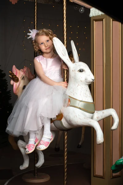 Mała dziewczynka w różowej sukience i korona na karuzeli z białym zającem — Zdjęcie stockowe