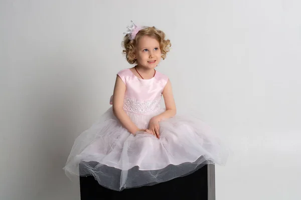 Mała dziewczynka w różowej sukience i koronie siedzi na czarnej kostce na białym tle — Zdjęcie stockowe