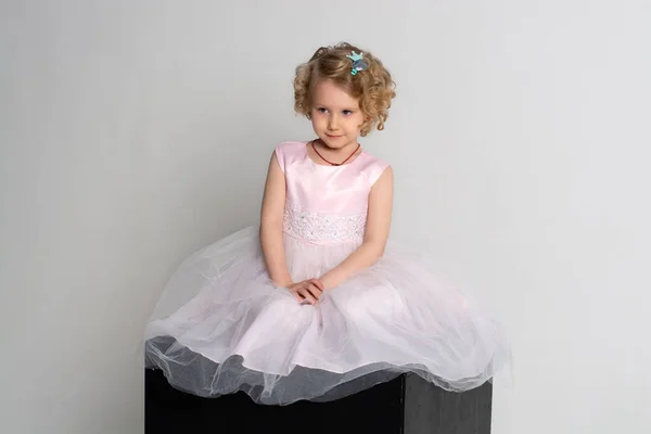 Uma menina em um vestido rosa e coroa senta-se em um cubo preto em um fundo branco — Fotografia de Stock