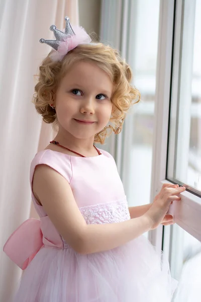 Mała Dziewczynka Różowej Sukience Korona Uśmiecha Się Przy Oknie — Zdjęcie stockowe