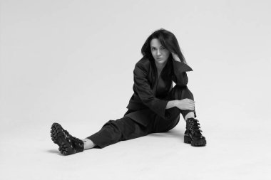 Beyaz bir arka planda oturan takım elbiseli bir kadın.