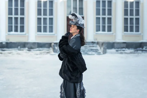 a woman dressed as a 19th-century noblewoman stands outside the castle.winter in russia