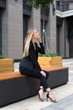 Şehirde siyah takım elbiseli sarışın bir kadın. Yürüyüş yapan bir iş kadını.