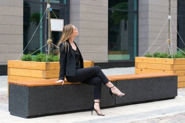 Şehirde siyah takım elbiseli sarışın bir kadın. Yürüyüş yapan bir iş kadını.