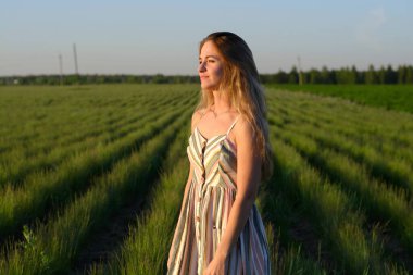 Gün batımında yeşil bir tarlada açık renk elbiseli bir kız.
