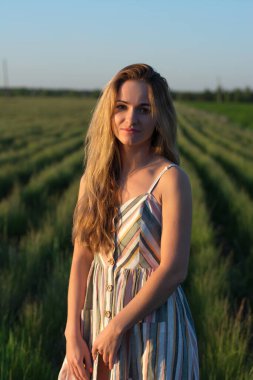 Gün batımında yeşil bir tarlada açık renk elbiseli bir kız.