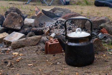 Taşların yanındaki siyah çaydanlık. Doğada yemek pişirmek.