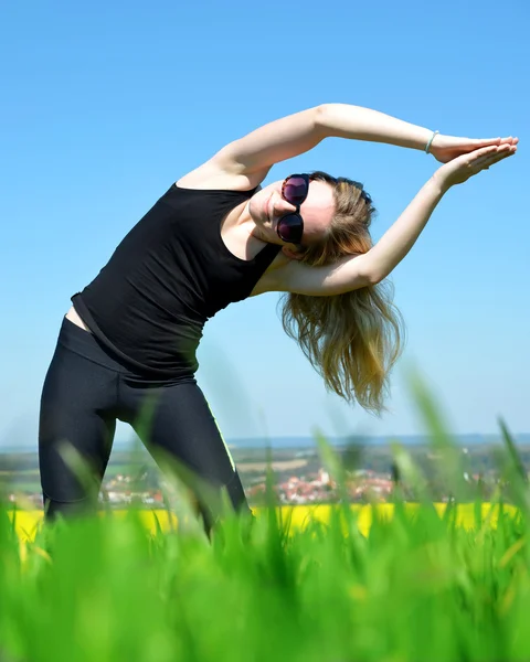 Young woman stretching on a meadow — Stock Photo, Image