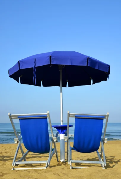 Ligstoelen en parasol op een zandstrand. — Stockfoto